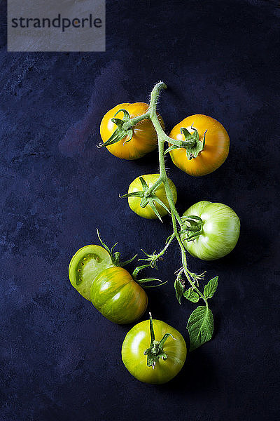 Ganze und in Scheiben geschnittene Tomaten 'Grünes Zebra' auf dunklem Grund