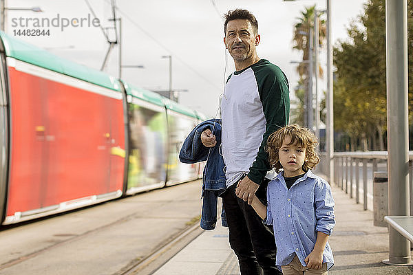 Vater und Sohn stehen Hand in Hand an der Straßenbahnhaltestelle in der Stadt