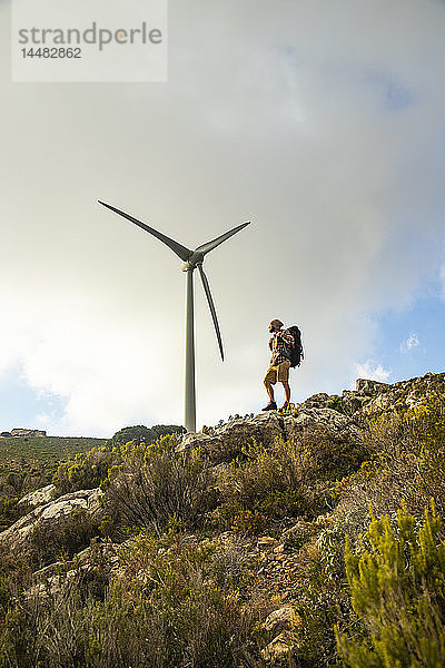 Spanien  Andalusien  Tarifa  Mann auf einer Wanderung auf einem Felsen stehend mit Windrad im Hintergrund