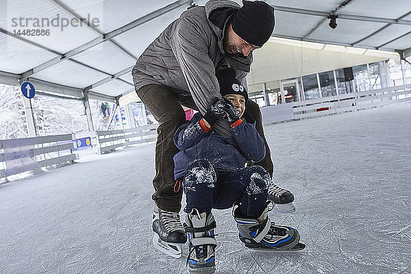 Vater und Sohn laufen gemeinsam Schlittschuh und haben Spaß auf der Eisbahn