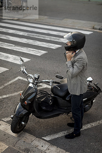 Geschäftsmann neben Motorroller  der einen Helm aufsetzt