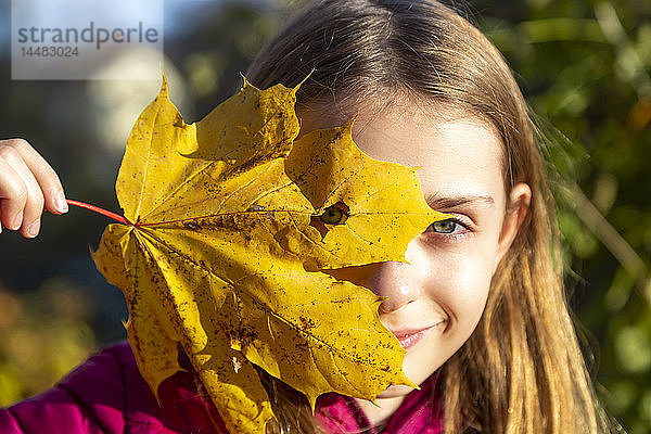 Porträt eines lächelnden Mädchens  das durch ein Loch im Herbstblatt blickt