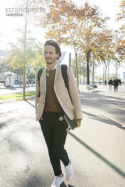 Porträt eines Mannes mit Rucksack und Skateboard in der Stadt im Herbst
