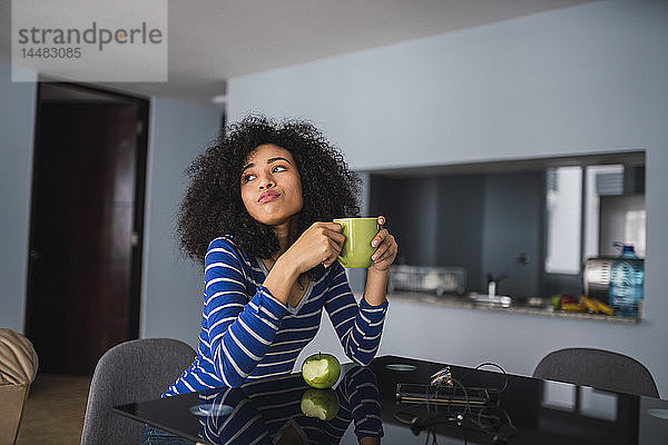 Porträt einer jungen Frau  die zu Hause Kaffee trinkt und einen Apfel isst