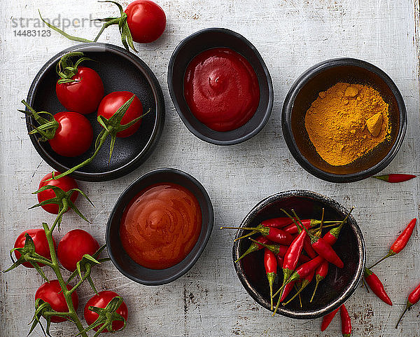 Tomaten  rote Chilischoten  Currypulver  Chili-Ketchup  Kurkuma und Tomatenketchup in Schalen