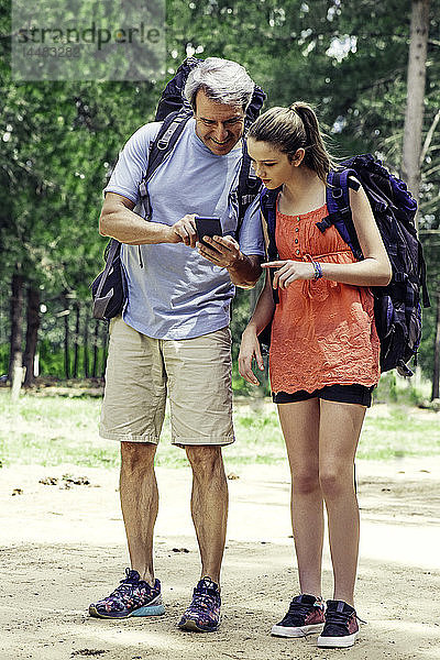 Vater und Tochter benutzen ein Smartphone im Wald