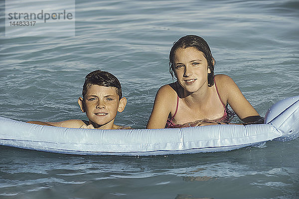 Lächelnder Bruder und Schwester schwimmen mit Schlauchboot
