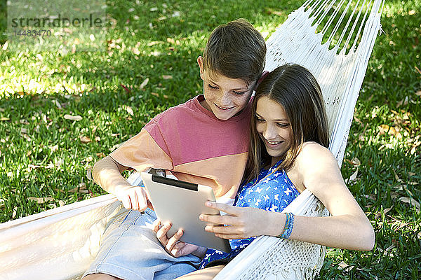 Bruder und Schwester benutzen ein digitales Tablet in einer Hängematte