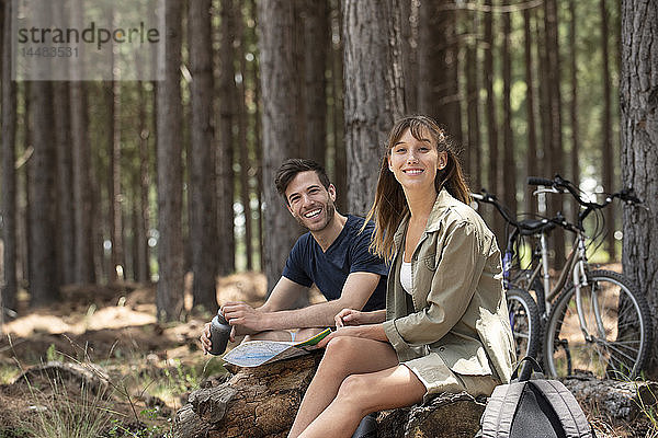 Lächelndes junges Paar sitzt auf einem Baumstamm im Kiefernwald