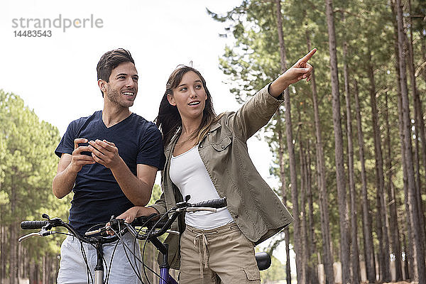 Junges Paar steht mit Fahrrädern im Kiefernwald