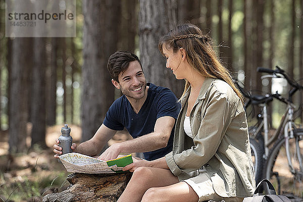 Lächelndes junges Paar  das im Wald sitzend eine Karte liest
