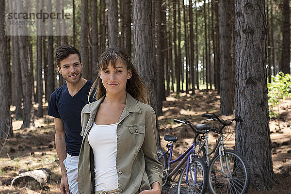 Lächelndes junges Paar im Kiefernwald stehend