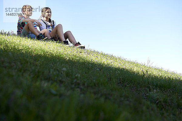 Bruder und Schwester sitzen auf einem Grashügel