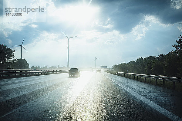 Sonne reflektiert auf nasser Autobahn Berliner Ring mit Windkraftanlagen in der Ferne  Berlin  Deutschland