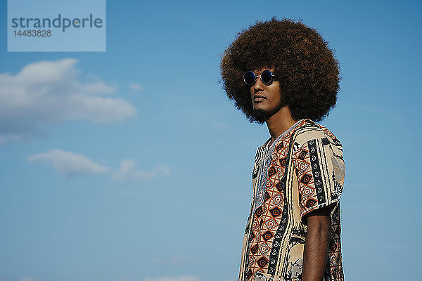 Junger Mann mit Afro gegen blauen Himmel stehend