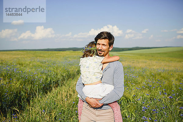 Porträt Vater hält Tochter in einem sonnigen  idyllischen ländlichen Feld mit Wildblumen