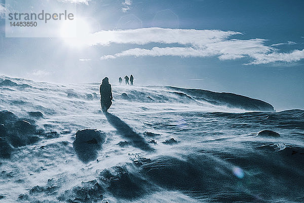 Menschen wandern durch eine sonnige  windige  schneebedeckte Landschaft  Reykjadalur  Island