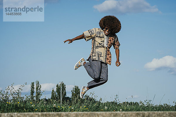Unbekümmerter junger Mann mit Afro  der vor Freude springt