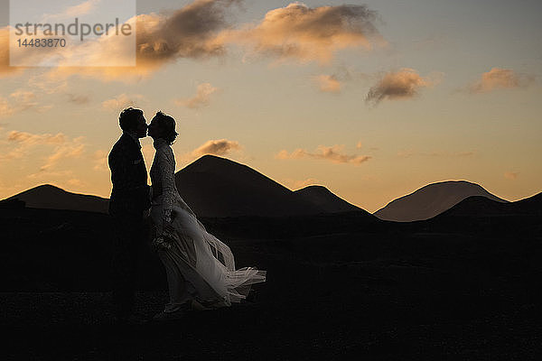 Silhouette Braut und Bräutigam küssen in der Abenddämmerung mit ruhigen Bergen im Hintergrund