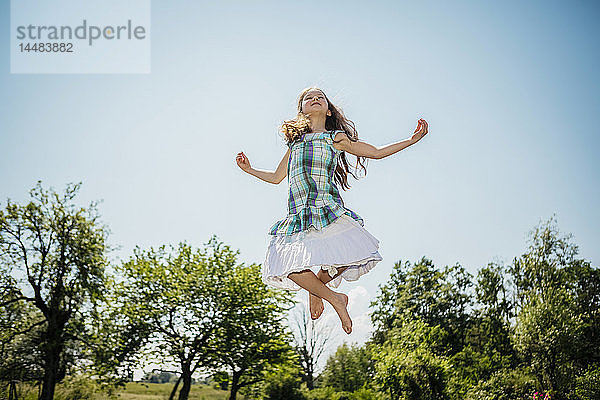 Unbekümmertes Mädchen im Kleid springt vor Freude im sonnigen Hinterhof