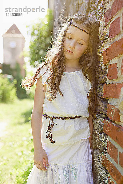 Gelassenes Mädchen im Kleid lehnt an einer Backsteinmauer