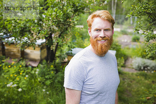 Porträt lächelnder  selbstbewusster Mann mit roten Haaren im Garten