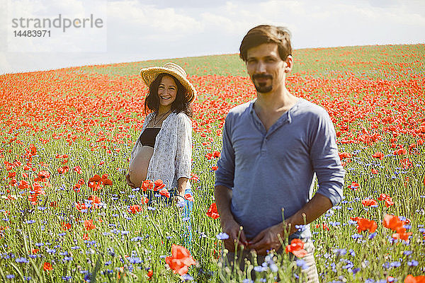 Porträt lächelnd schwangeres Paar in sonnigen  idyllischen ländlichen roten Mohnfeld