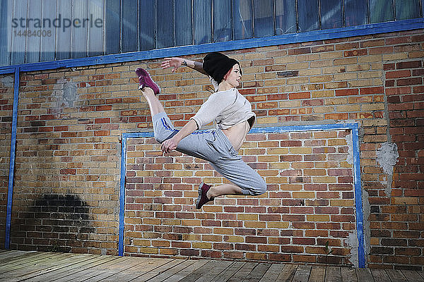 Weibliche moderne Tänzerin  die gegen eine Backsteinmauer tanzt