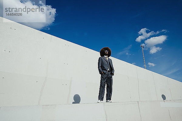 Porträt selbstbewusster  cooler  gut gekleideter junger Mann mit Afro  der an einer städtischen Wand steht