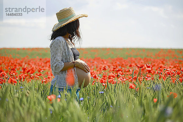 Schwangere Frau in einem sonnigen  idyllischen ländlichen Feld mit rotem Mohn