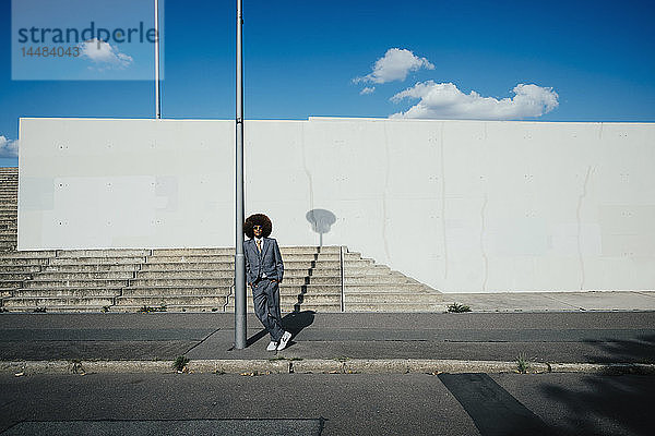 Porträt eines selbstbewussten  coolen  gut gekleideten jungen Mannes mit Afro auf einem städtischen Bürgersteig