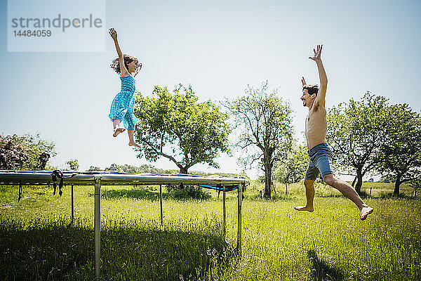 Verspielter Vater und Tochter springen auf dem Trampolin im sonnigen Sommergarten