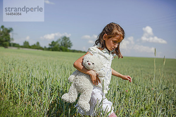 Mädchen mit Teddybär auf sonniger  grüner Wiese im ländlichen Raum