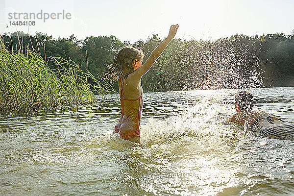 Verspieltes Mädchen planscht und Frau schwimmt im sonnigen Sommersee