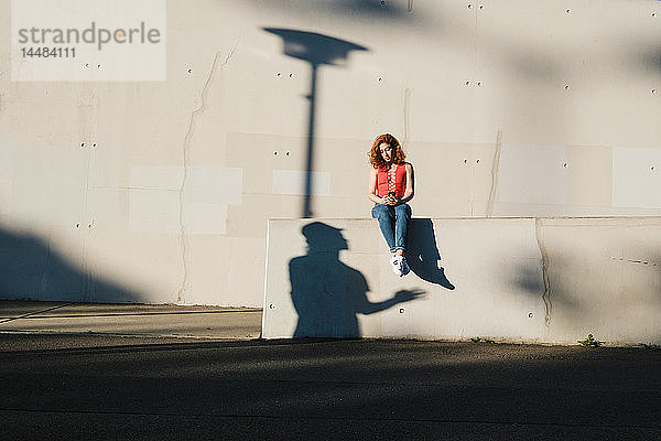 Schatten  der zu einer jungen Frau aufblickt  die ein Smartphone an einer Hauswand benutzt