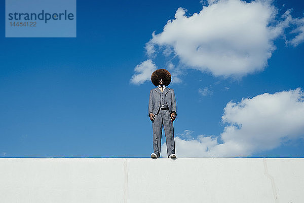 Porträt selbstbewusster  cooler  gut gekleideter junger Mann mit Afro an der Wand stehend gegen den Himmel