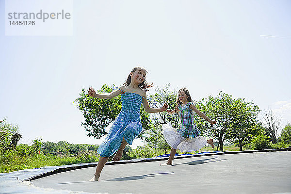 Verspielt  sorglos barfuß Mädchen in Kleidern spielen auf Trampolin in sonnigen Hinterhof