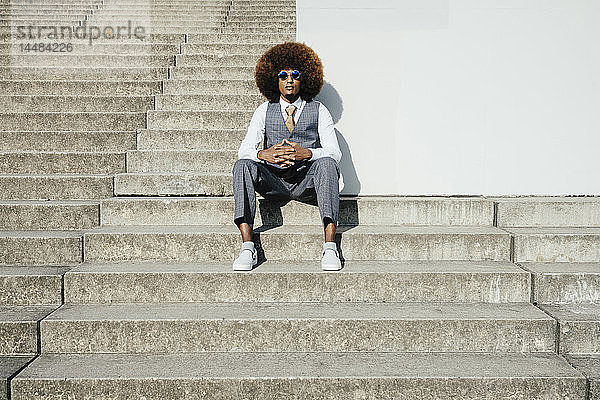 Porträt selbstbewusster  cooler  gut gekleideter junger Mann mit Afro  der auf städtischen Stufen sitzt