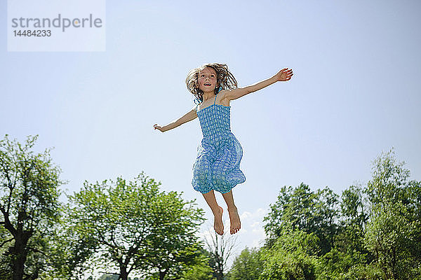 Unbekümmertes Mädchen im Kleid springt vor Freude im sonnigen Hinterhof