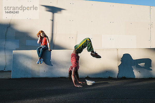 Junge Frau beobachtet Mann machen Handstand entlang städtischen Wand