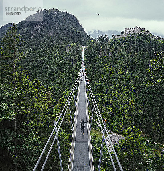 Menschen gehen über eine Hängebrücke über grüne Baumkronen  Tirol  Österreich