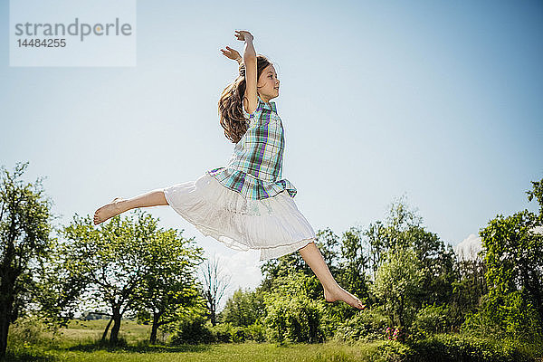 Unbekümmertes Mädchen im Kleid springt vor Freude im sonnigen Hinterhof