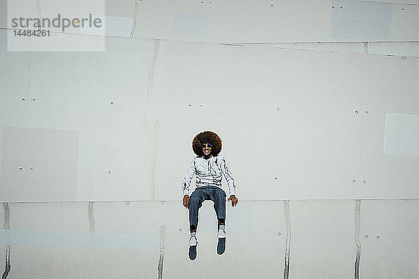 Porträt glücklicher junger Mann mit Afro an der Wand sitzend