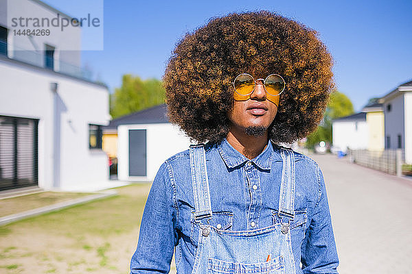 Portrait cooler junger Mann mit Afro in Jeans-Overall auf sonniger Straße stehend