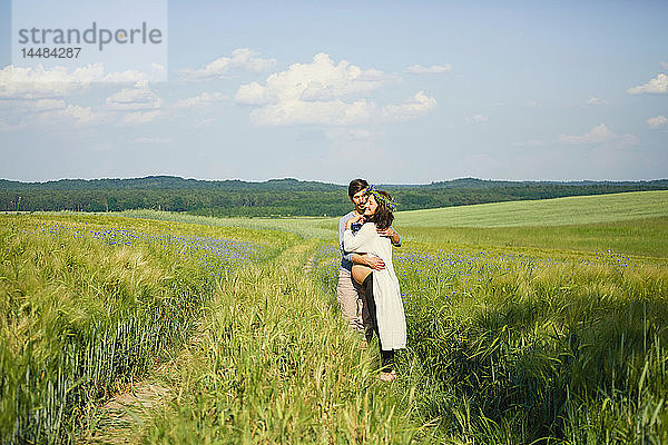 Zärtliches schwangeres Paar  das sich auf einer sonnigen  idyllischen  grünen Wiese umarmt