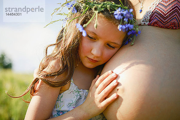 Serene Mädchen mit Blumen im Haar lehnt auf schwangere Mütter Bauch