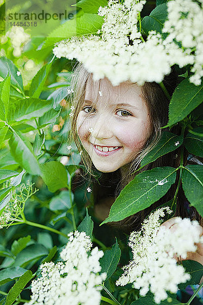 Porträt lächelndes Mädchen versteckt sich in blühendem Busch