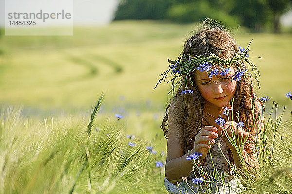 Neugieriges Mädchen mit Wildblumen im Haar in einem sonnigen  ländlichen Weizenfeld