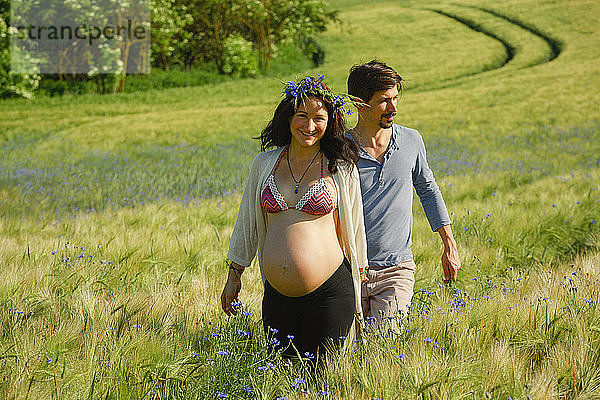 Porträt glückliches schwangeres Paar beim Spaziergang in einem sonnigen  idyllischen Feld mit Wildblumen