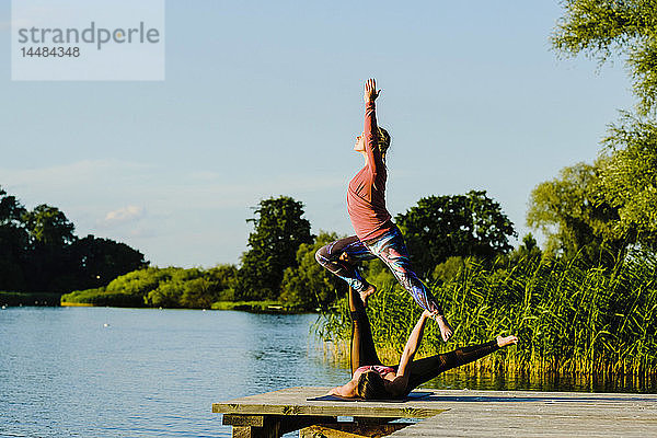 Frauen üben Acroyoga auf einem sonnigen Steg am See